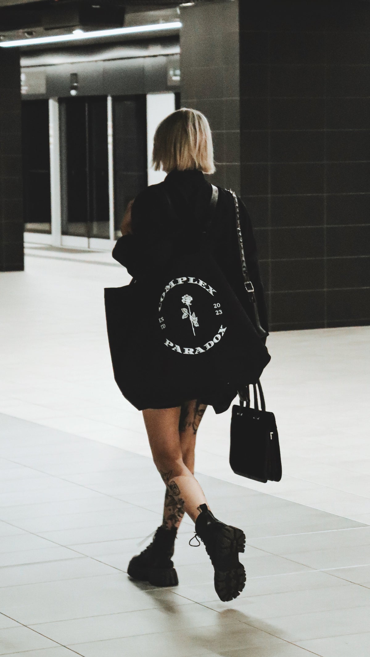 Model carrying a black Complex Paradox tote bag with graphic logo print