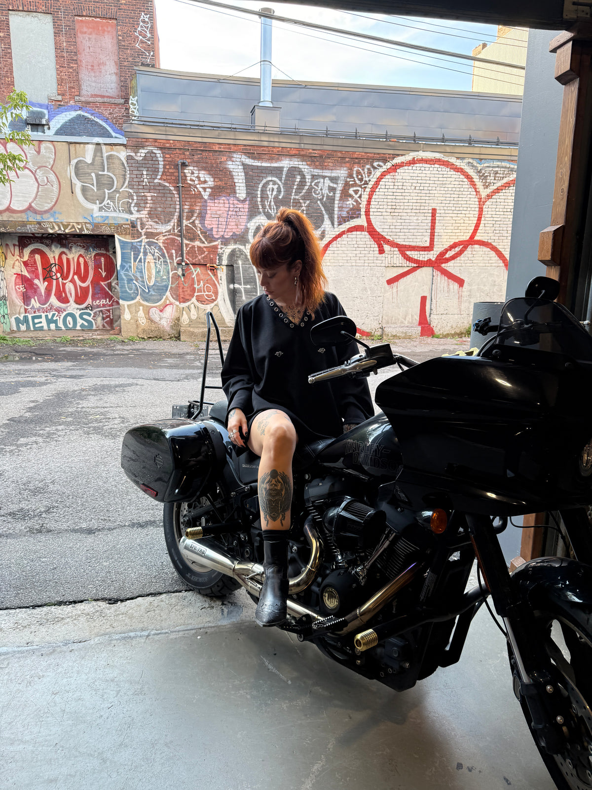 Model in all-black CMPLX look seated on motorcycle in graffiti alley, Complex Paradox lookbook